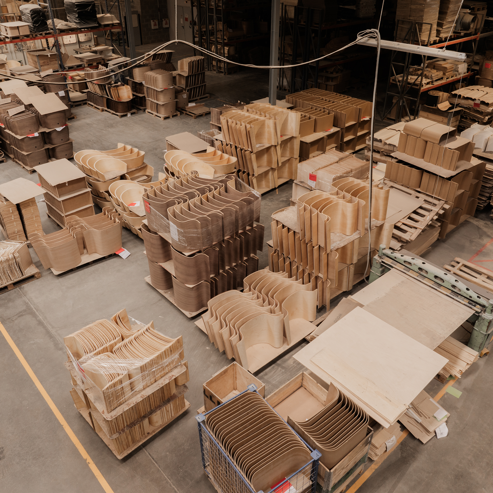 Warehouse interior with neatly stacked piles of wooden components and sheets. Aisles and overhead lighting visible.