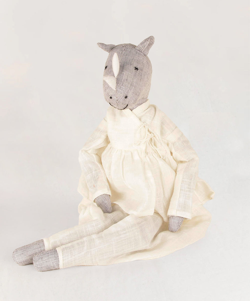 Le Rhino, a stuffed animal featuring a rhino-like head in a white garment, is positioned against a plain backdrop.