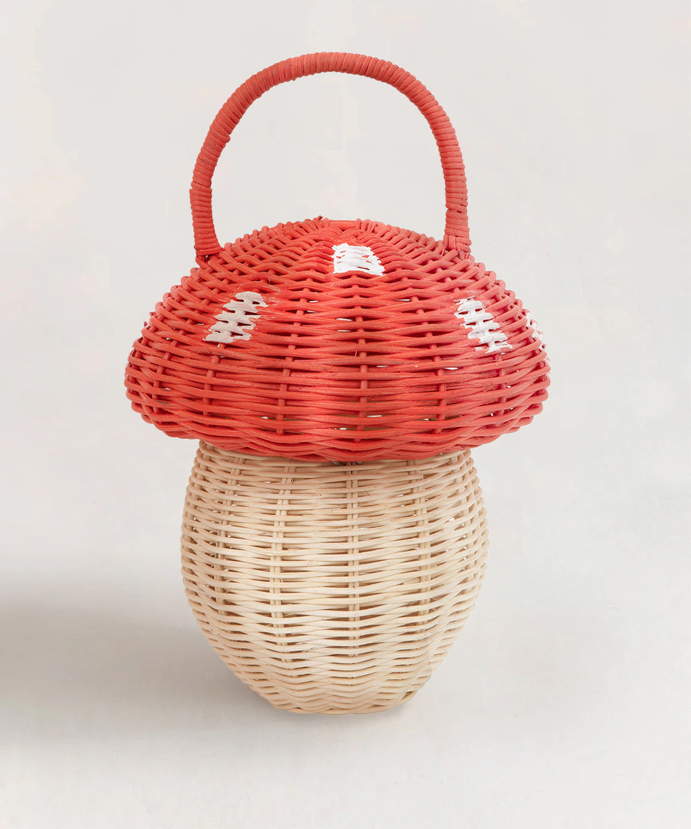 The Mushroom Basket is a woven basket shaped like a mushroom, featuring a red cap with white spots and a curved handle on top.