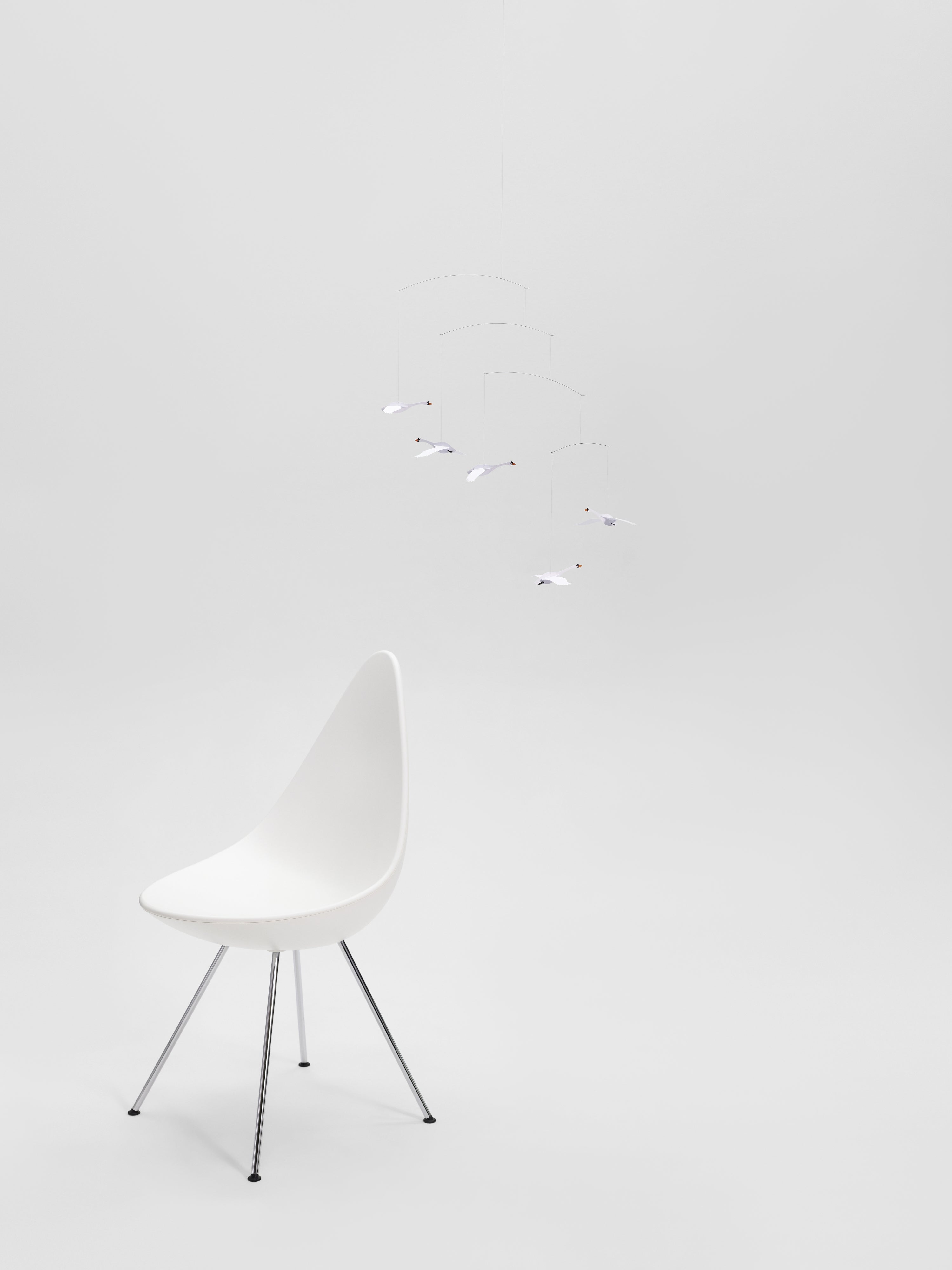 The Scandinavian Swans modern white chair sits on a plain background beneath a minimal hanging mobile.