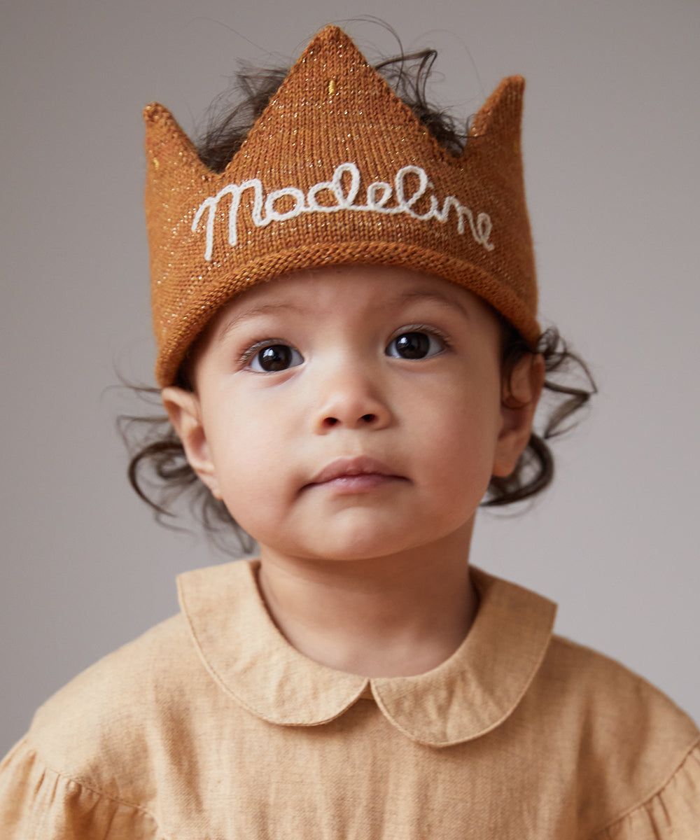 Toddler wearing a Personalized Gold Crown - Light Pink with "Madeline" embroidered, paired with a matching collared shirt, looking at the camera.