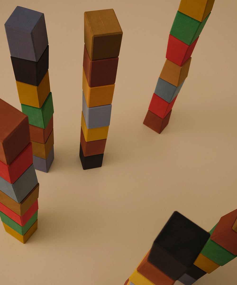 Le Oddy Cubes - Mini: Colorful wooden cubes stacked into tall towers on a beige surface, seen from above.