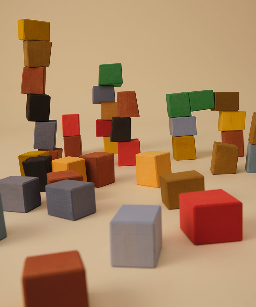 Le Oddy Cubes - Mini: colorful wooden blocks stacked and scattered on a beige surface with a plain beige background.