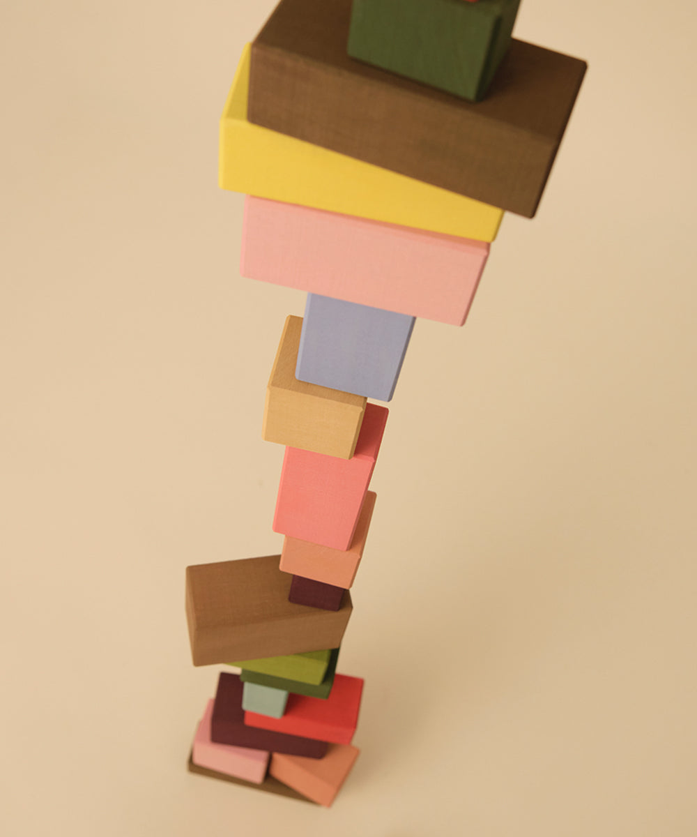 Le Rectangles: A tall stack of colorful, unevenly balanced wooden blocks on a beige background, viewed from above.