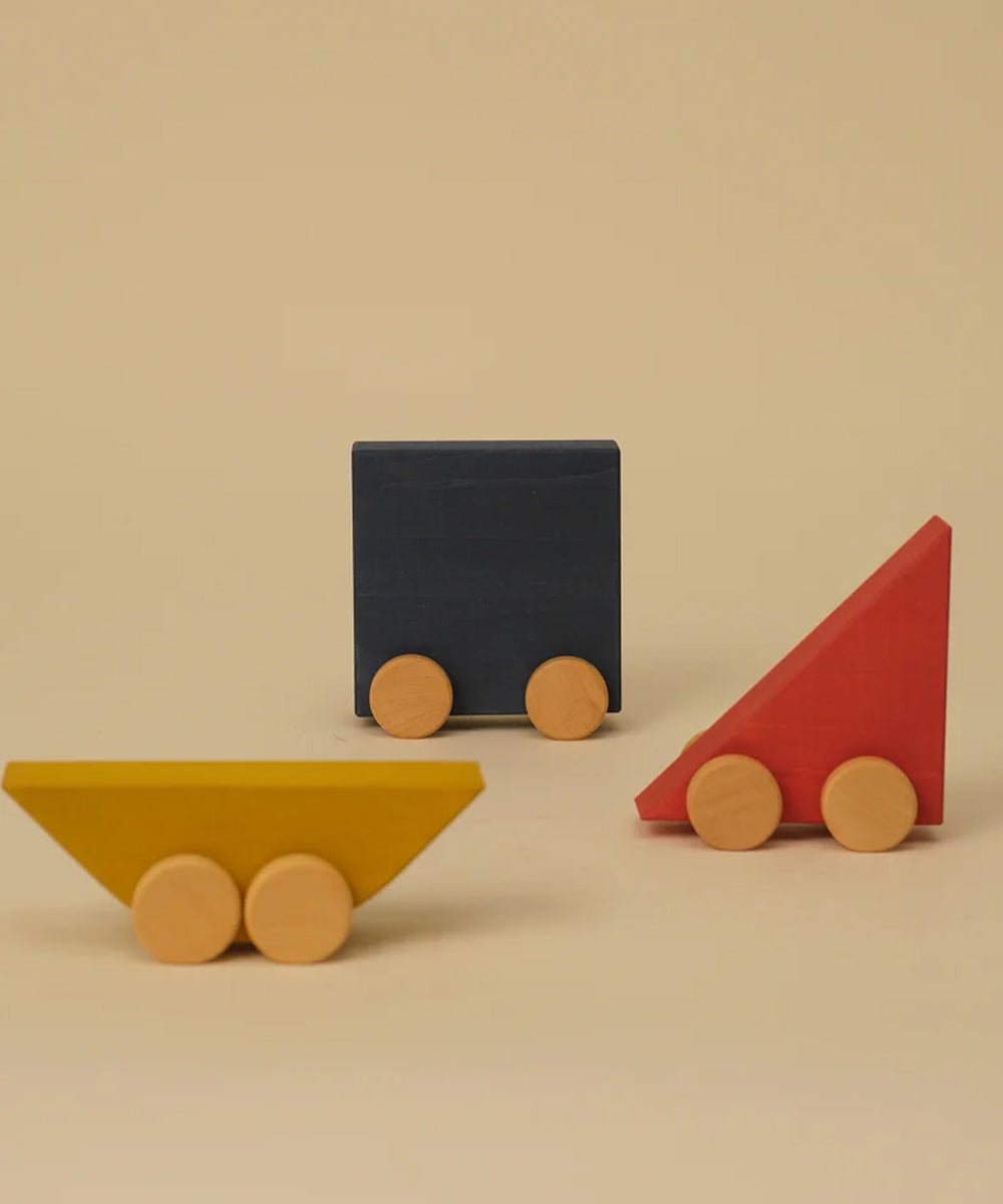 Le Vehicle Trio: a set of three wooden toy vehicles in blue, yellow, and red, each with two wooden wheels, displayed on a beige background.