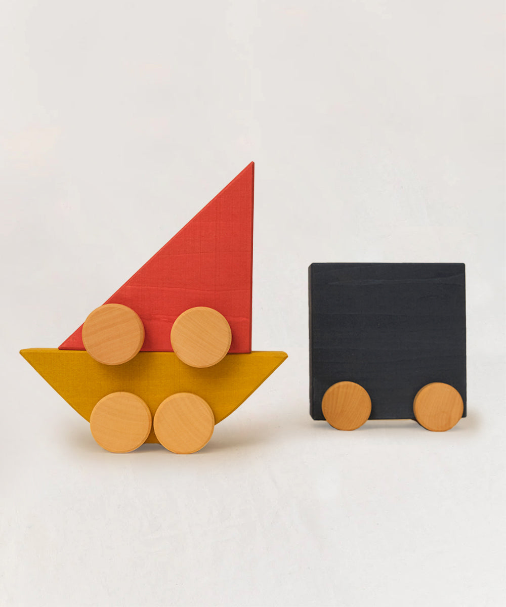 Le Vehicle Trio features red sailboat and black truck wooden shapes, each with round wheels, set against a plain background.