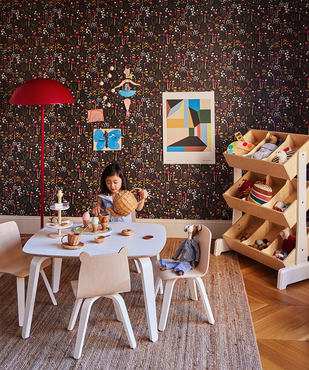 A child plays at a small table with toy food in a colorful playroom. A bookshelf filled with toys stands against a patterned wall, adorned with the Le Collage One Poster artwork.