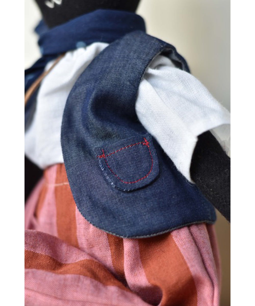 Theo le Skunk is a cloth doll dressed in a blue vest, white shirt, and red striped skirt with visible stitching.