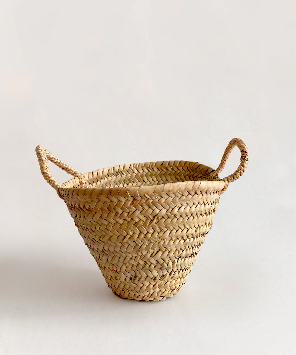 The Le Market Basket - Small is crafted from natural fibers and features two handles, showcased against a neutral backdrop.