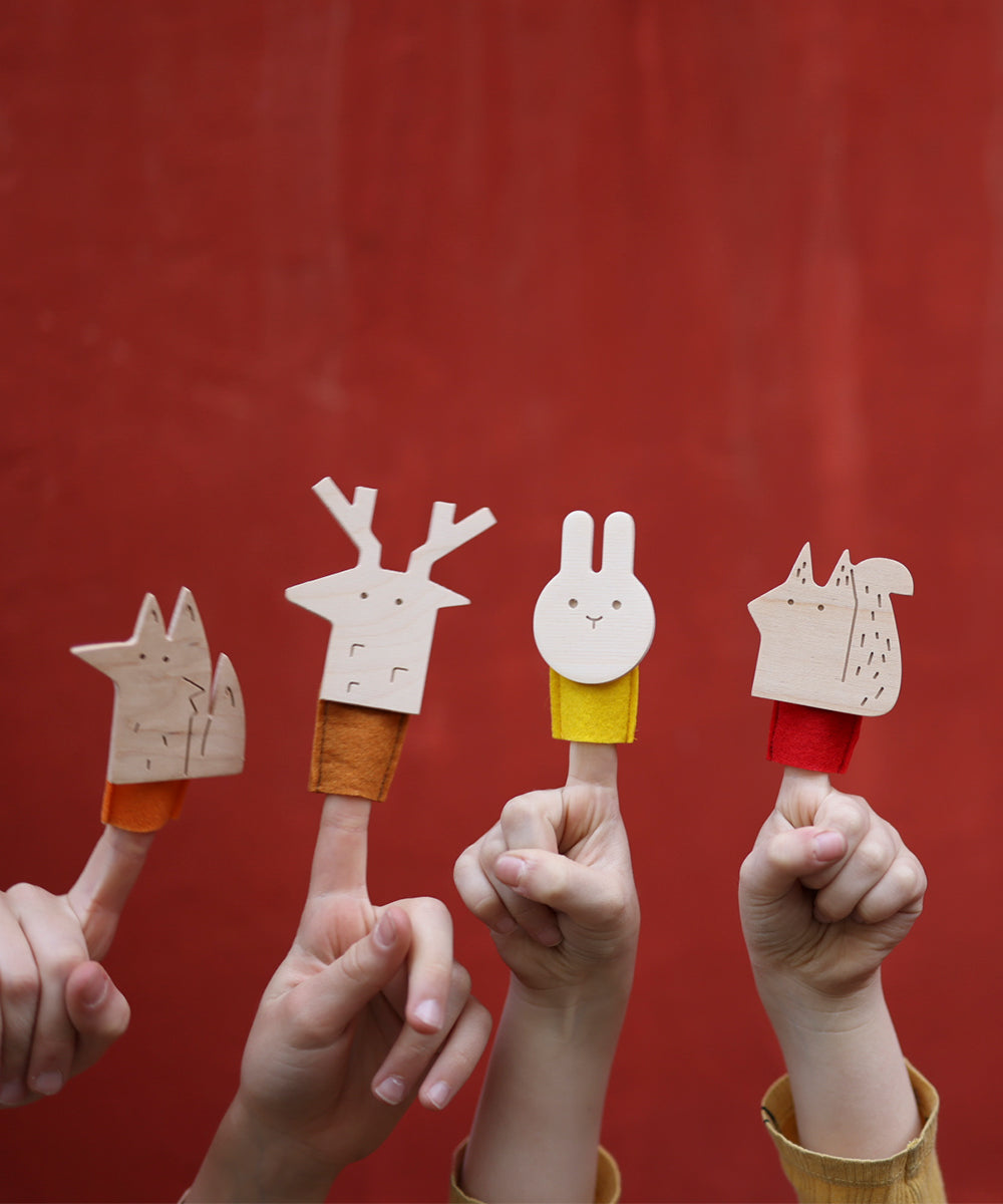 Four hands each hold a Le Rabbit Finger Puppet shaped like different animals against a red background.