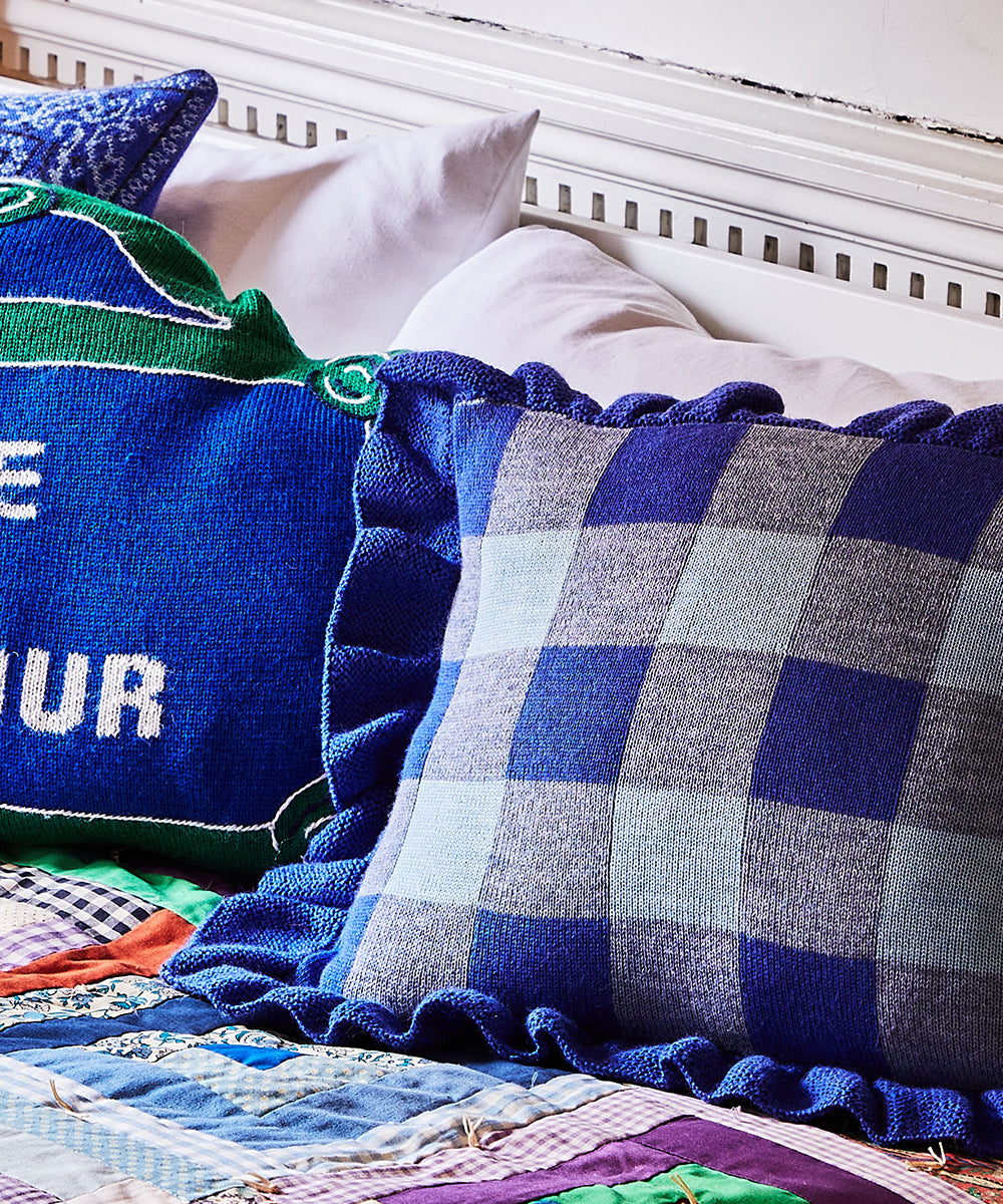 A bed with a Gingham Ruffle Pillow in blue checkered pattern and another pillow featuring text in blue and green.