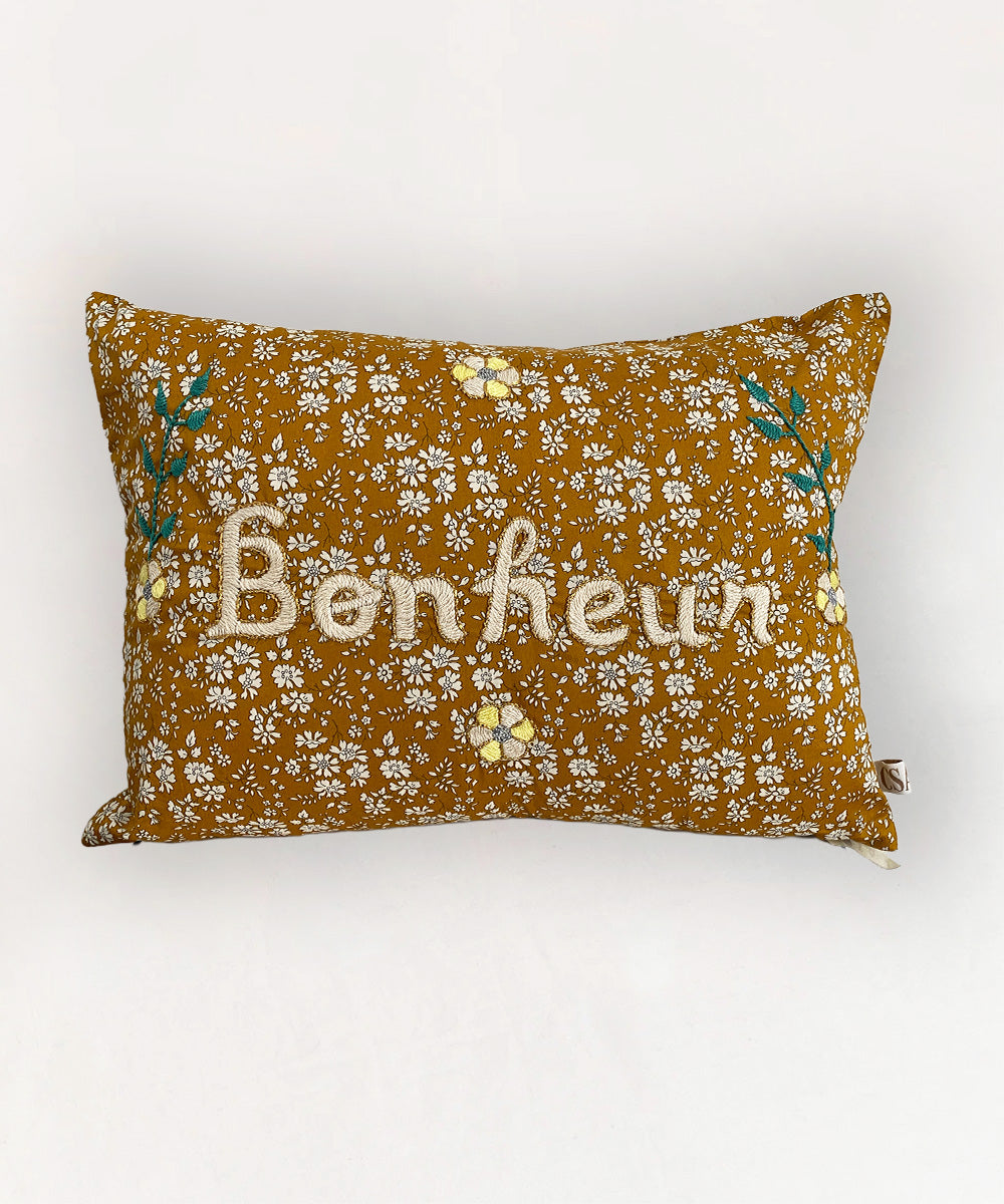 Le Embroidered Pillow - Floral Bonheur: Rectangular mustard pillow with white floral pattern and "Bonheur" embroidered on the front.