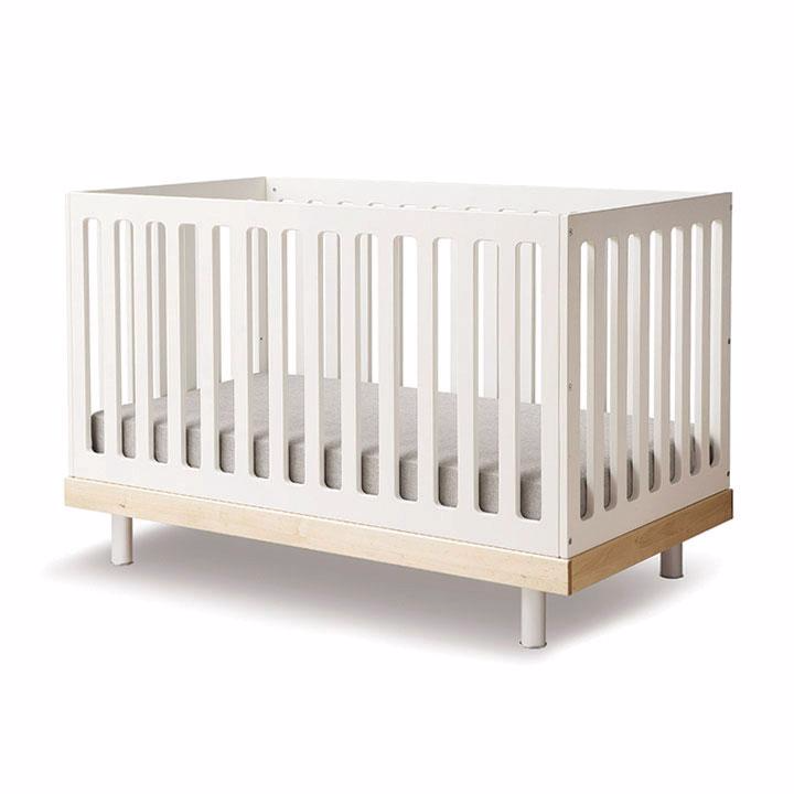 White baby crib with vertical slats and a light wooden base, featuring a gray mattress.