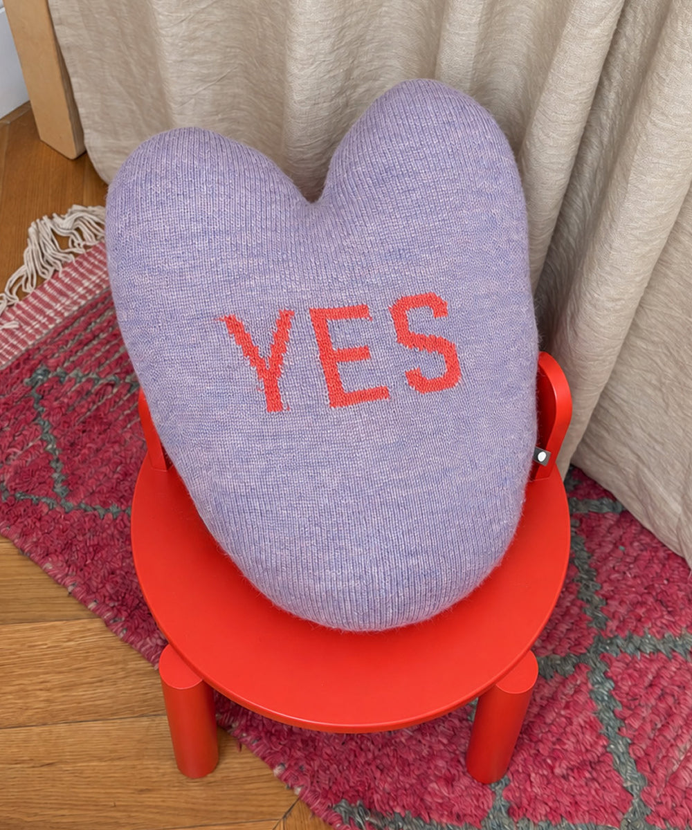 Yes/No Heart Pillow: a lavender heart-shaped pillow with the word “YES” embroidered in red, resting on a small red stool.