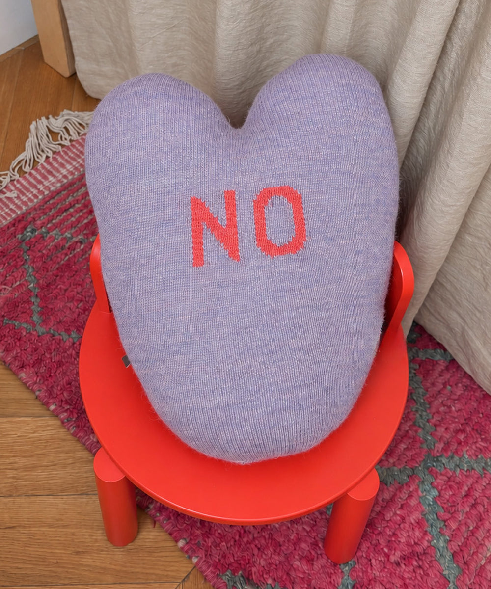 Yes/No Heart Pillow: a heart-shaped lavender knit pillow with the word “NO” in red letters, resting on a small red stool.