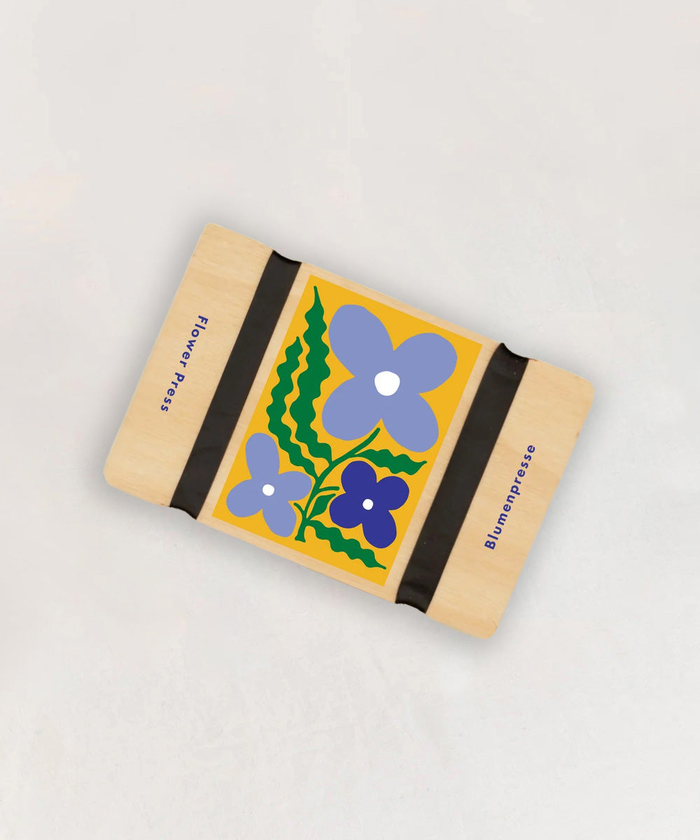 Le Pocket Flower Press: a wooden flower press with straps and a colorful floral illustration on top.