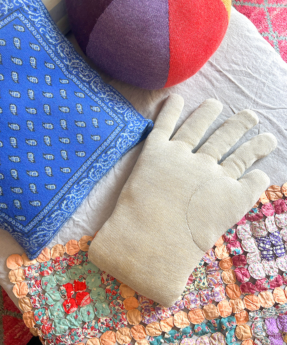 A Hand Pillow with beige, blue patterned, and colorful patchwork fabric rests on a light surface.