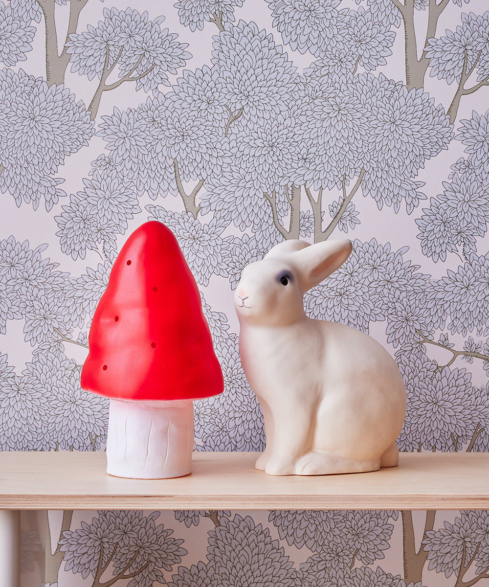 The Le Bunny Lamp and a red mushroom lamp sit on a wooden shelf against floral wallpaper.