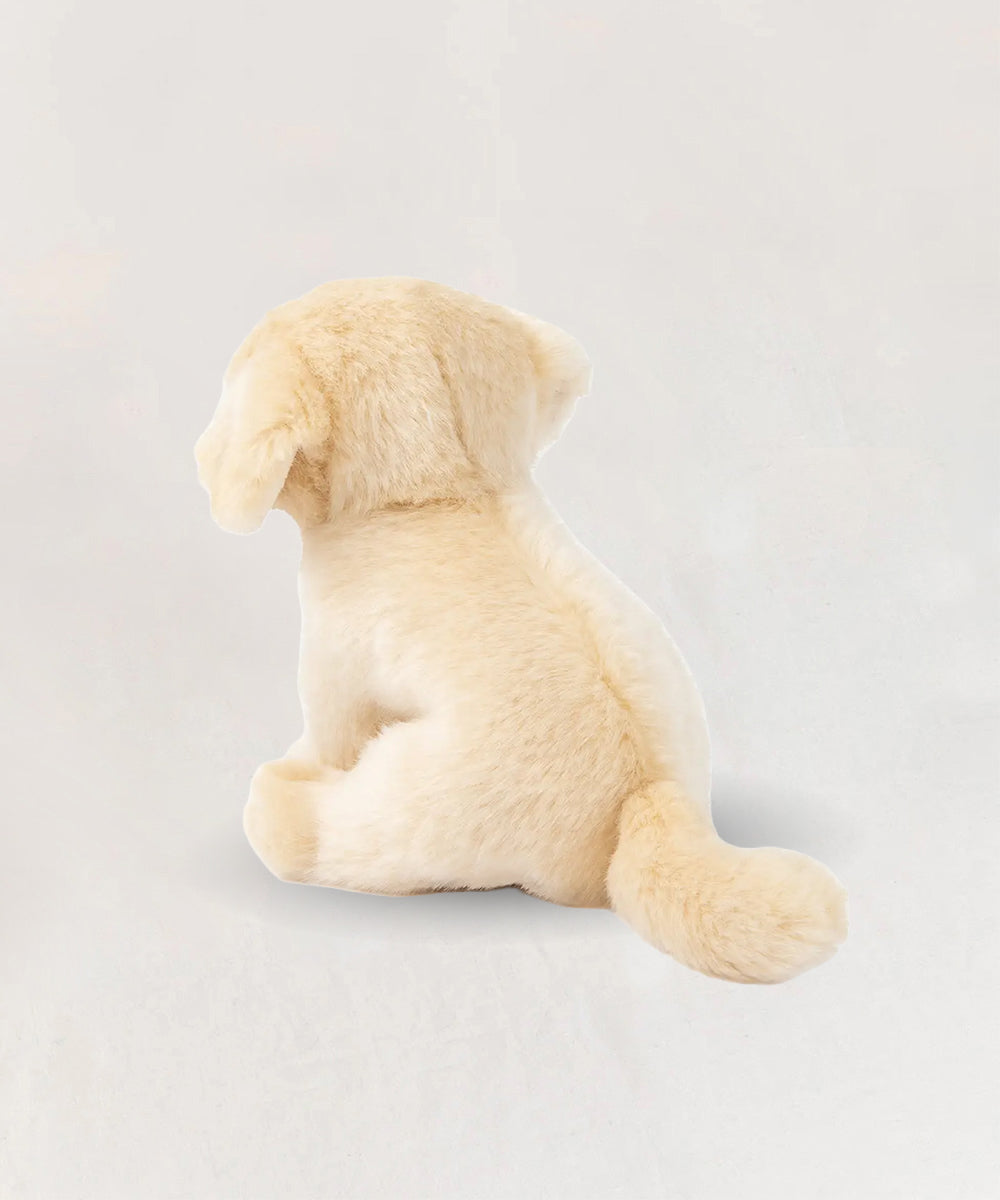 Loulou le Labrador, a light beige plush puppy toy, sits facing away on a plain white background.