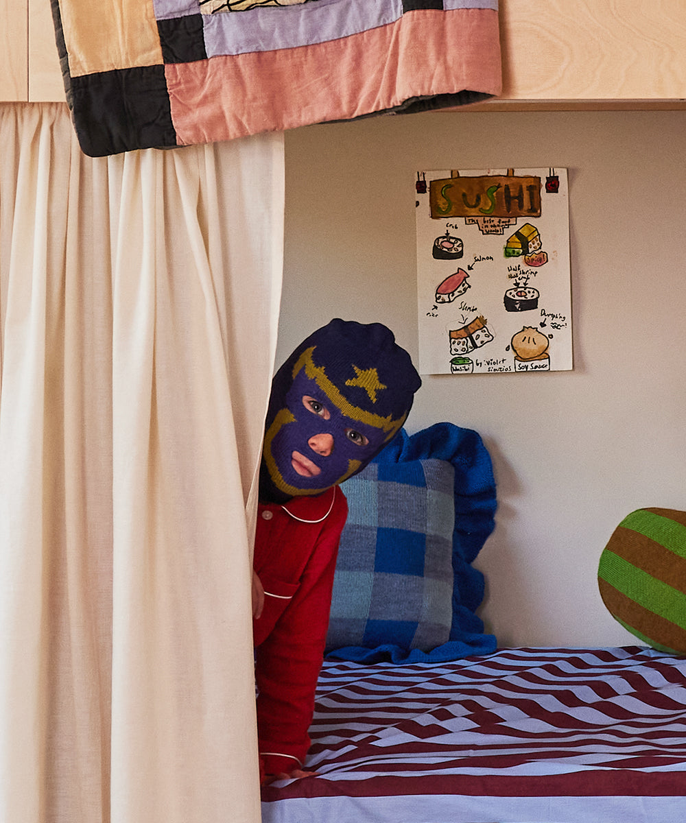 A person in a Luchador Mask peeks from behind a bunk bed curtain beside a sushi-themed poster on the wall.