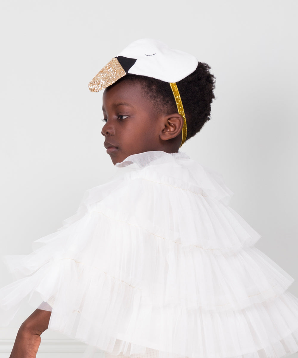 Child wearing a Swan Costume, featuring a white ruffled cape and a swan mask with a gold beak, looking to the side.