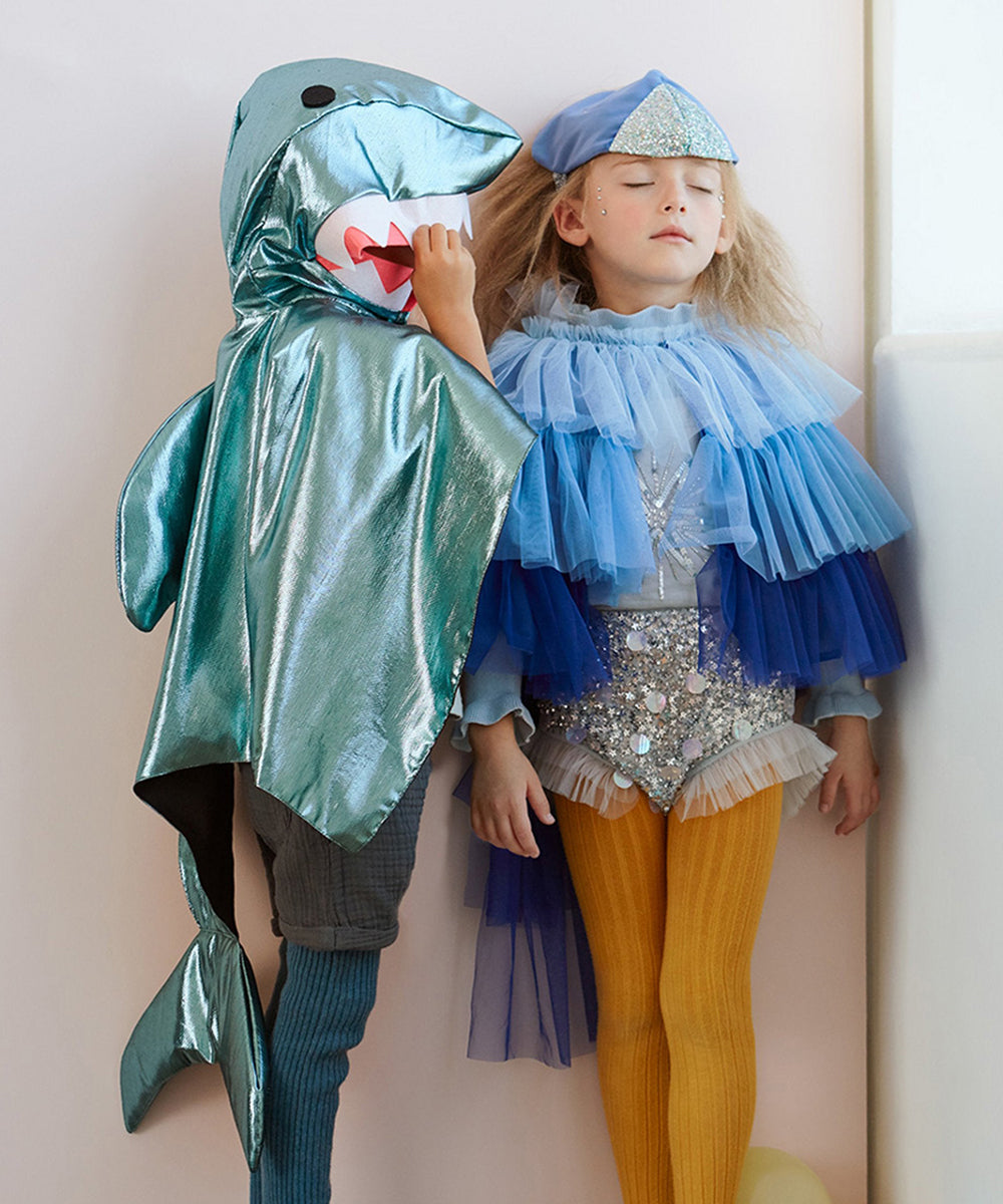 Child in a Shark Costume stands beside another child dressed in a blue ruffled outfit with yellow tights.