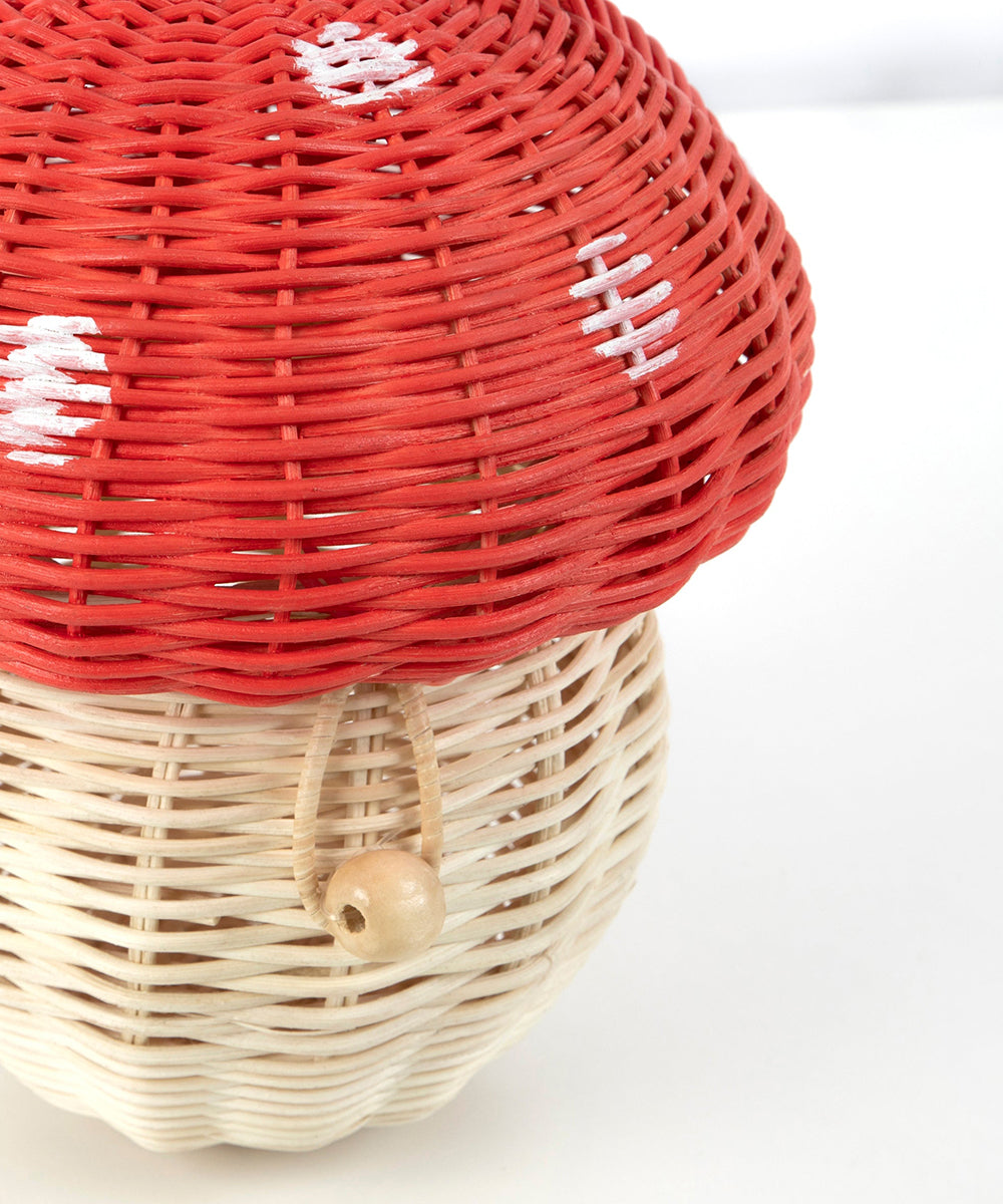 The Mushroom Basket is a woven basket shaped like a red and white mushroom with a wooden bead on the front.