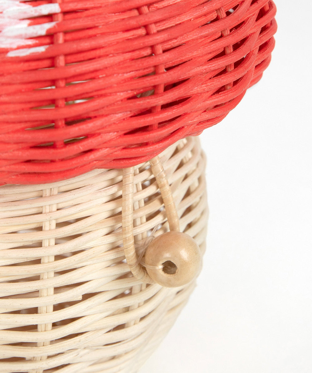 Close-up of the Mushroom Basket, featuring red and beige woven wicker and a wooden bead attached by a loop.