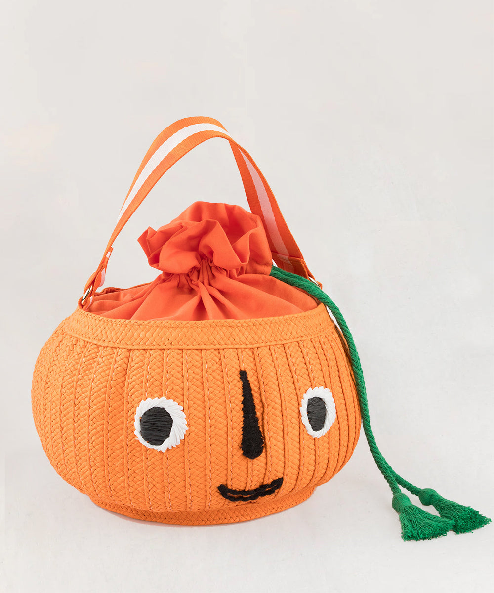 The Le Pumpkin Basket Bag is a pumpkin-shaped orange bag with a smiling face, green drawstring, and orange strap on a light background.