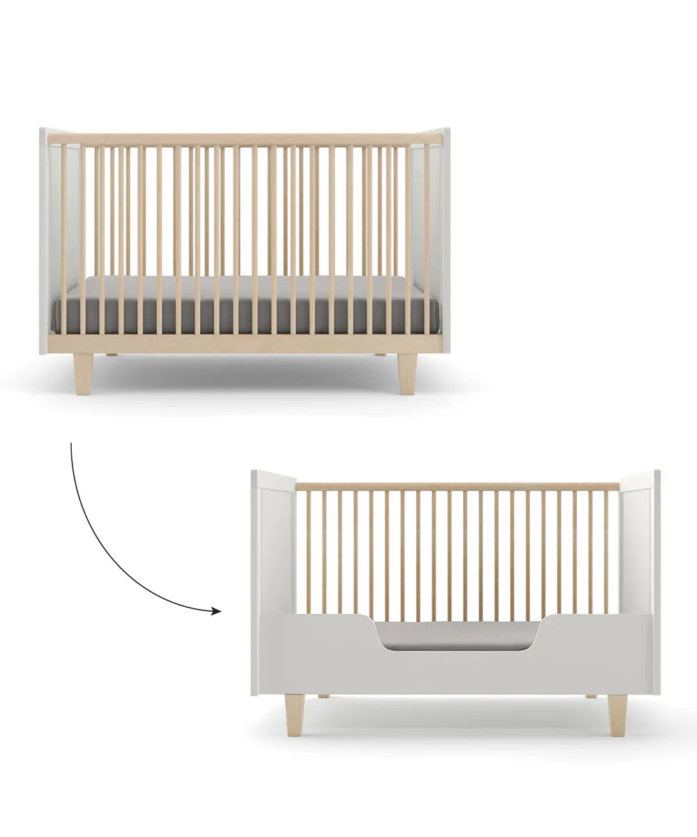 The Rhea Crib is featured in two stages: as a full crib and transitions seamlessly to a toddler bed using the Rhea Toddler Bed Conversion Kit. It boasts a light wood finish with white panels and a grey mattress, with an arrow emphasizing the smooth transformation.