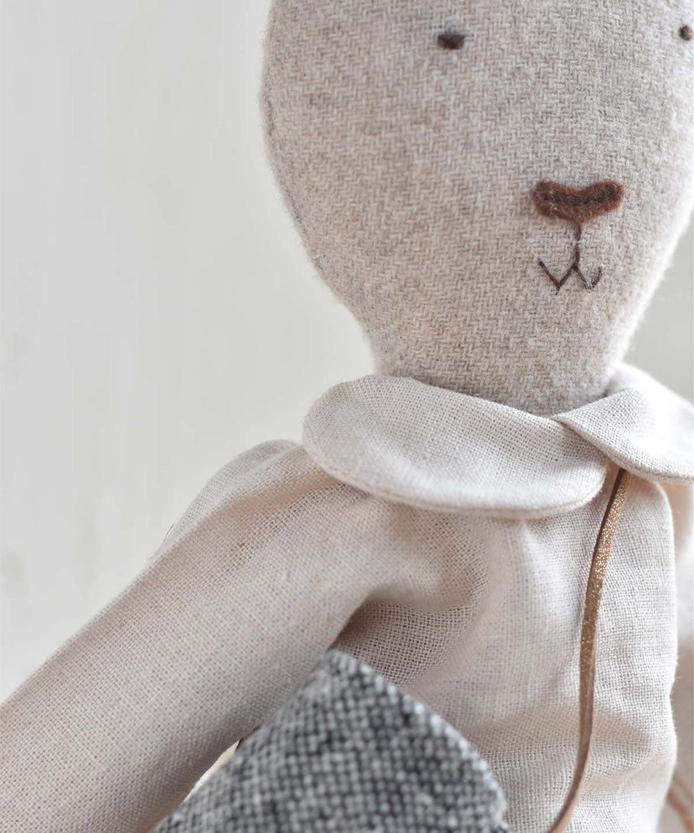 A close-up of Ruthie le Rabbit – Linen Dress, a fabric stuffed animal with embroidered facial features and a white collar.