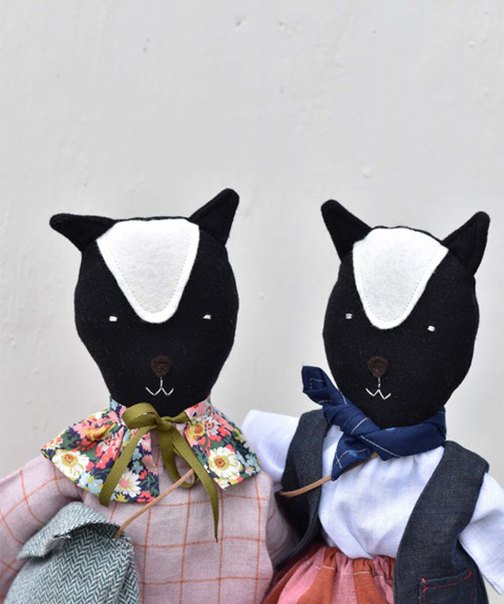 Two handmade Scout le Skunk fabric dolls dressed in colorful outfits with bow ties and floral patterns.