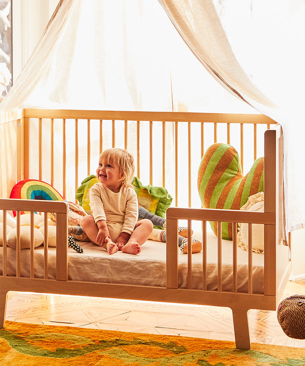 A cheerful toddler sits in a Sparrow with rainbow-themed pillows and a canopy overhead.