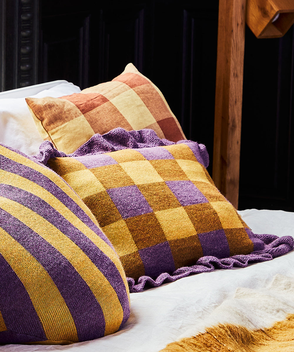 Close-up of a bed with Gingham Ruffle Pillows featuring orange, brown, and purple plaid against a dark ornate headboard.