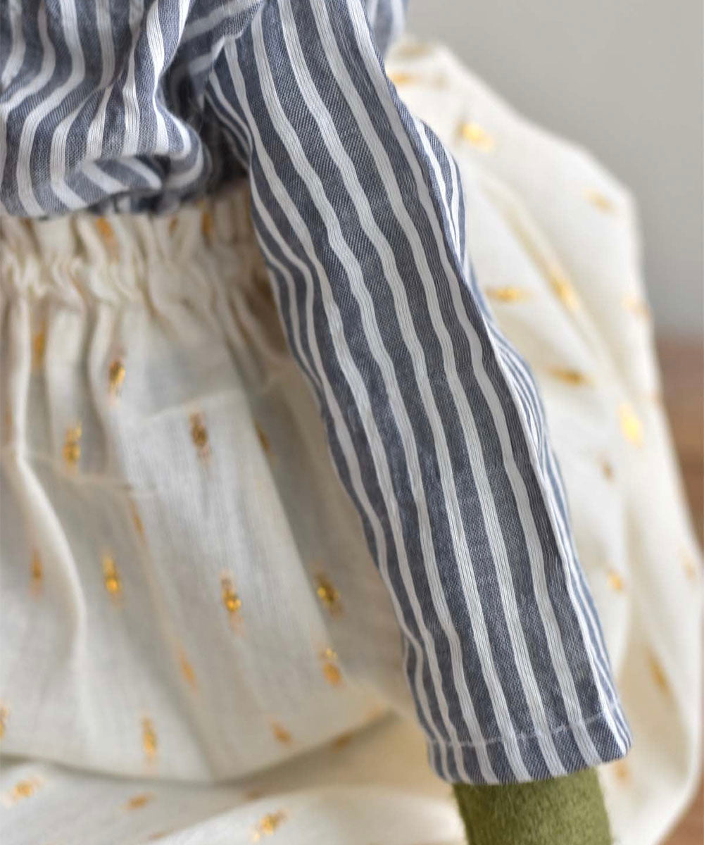 A close-up of the Fern le Frog doll wearing a blue-and-white striped shirt and a white sparkle skirt with gold dots.