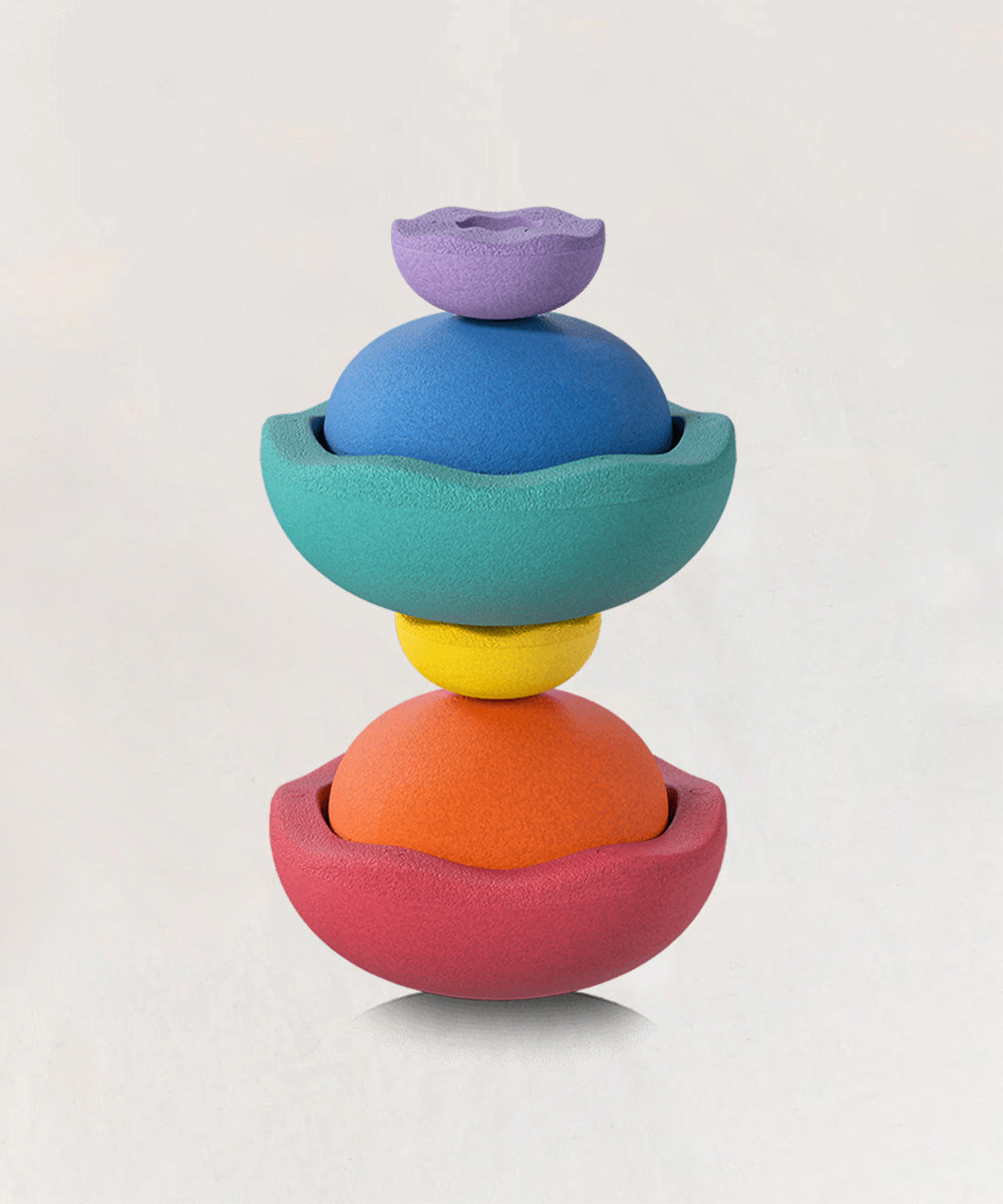 Four semi-spherical Le Inside Rainbow toys, colorful and textured, are stacked against a light background.