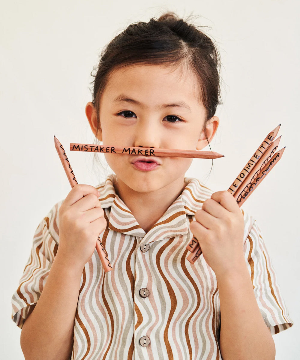 A young girl wearing a wavy striped shirt playfully holds Le Mistake Maker Pencils, including one labeled "MISTAKER MAKER".